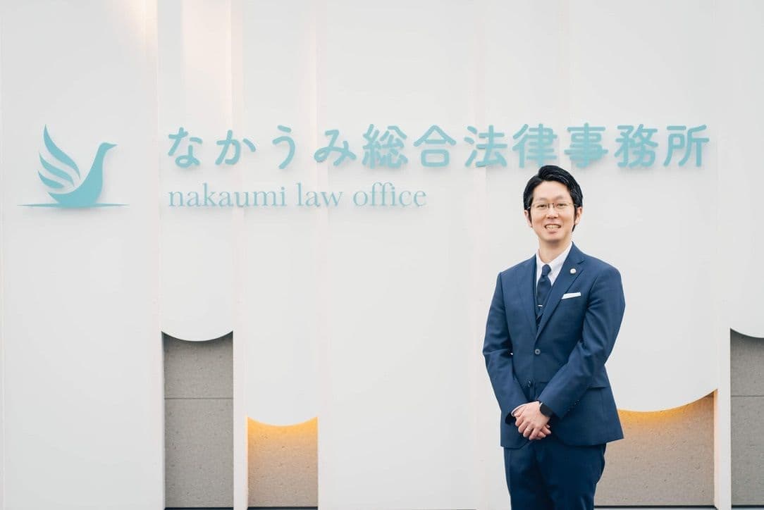 米子市にある「なかうみ総合法律事務所」の建物看板前で、代表弁護士の百毛公平(ももけこうへい)が撮影された写真。清潔感あるスーツ姿で微笑む表情からは、依頼者に寄り添い誠実に向き合う姿勢が伝わり、地域に根ざした信頼できる法律事務所であることを象徴しています。背景には事務所のシンボルロゴと「なかうみ総合法律事務所」の看板が映し出され、法律相談に訪れる方へ安心と信頼を与える存在感を示しています。なかうみ総合法律事務所は、米子市を中心に相続、離婚、交通事故、債務整理、企業法務など幅広い法律相談に対応し、代表弁護士 百毛公平をはじめとするスタッフが、依頼者の人生や事業を支える法的パートナーとして歩み続けています。